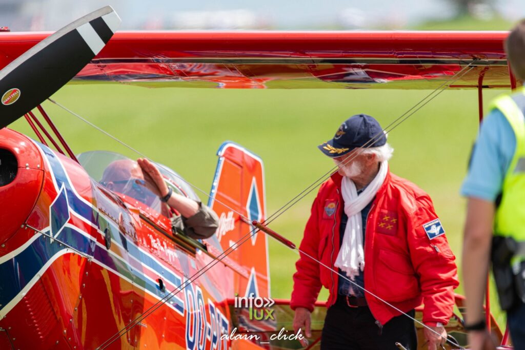 Photo de Jack Krine : Jack Krine, en blouson rouge et casquette, entouré de passionnés d'aviation devant un avion historique.